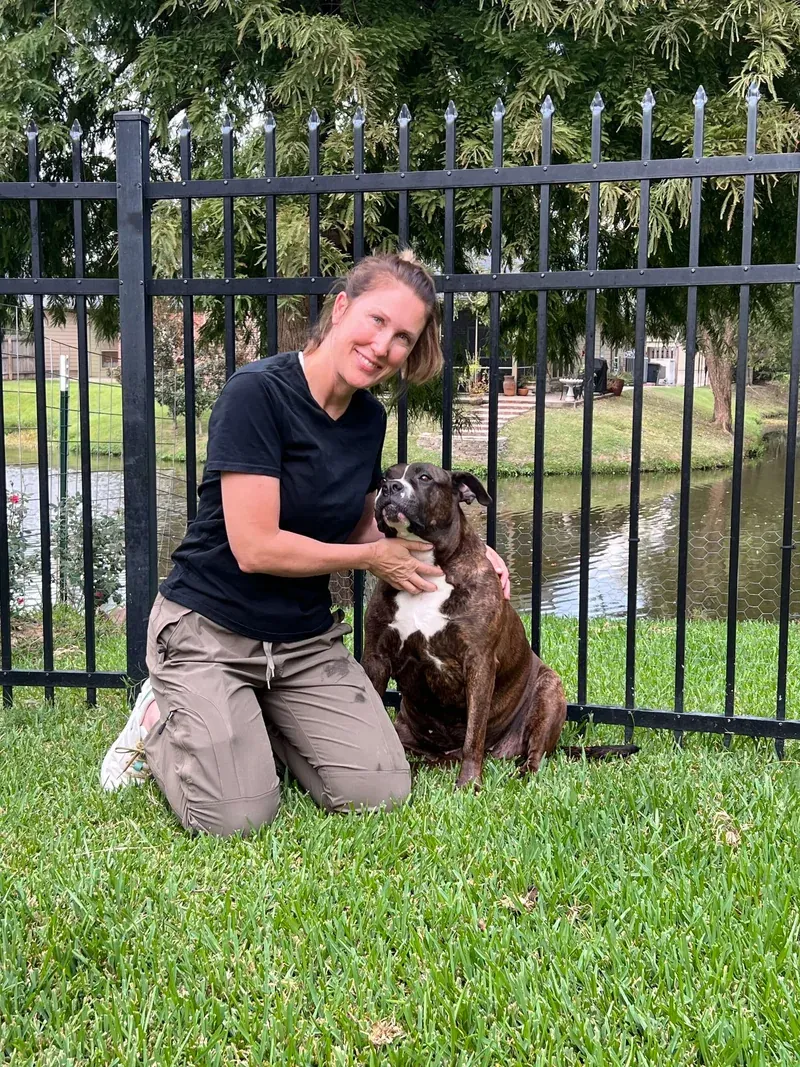 Amy VanHouten kneeling on the grass beside a brindle rescue dog looking up at her