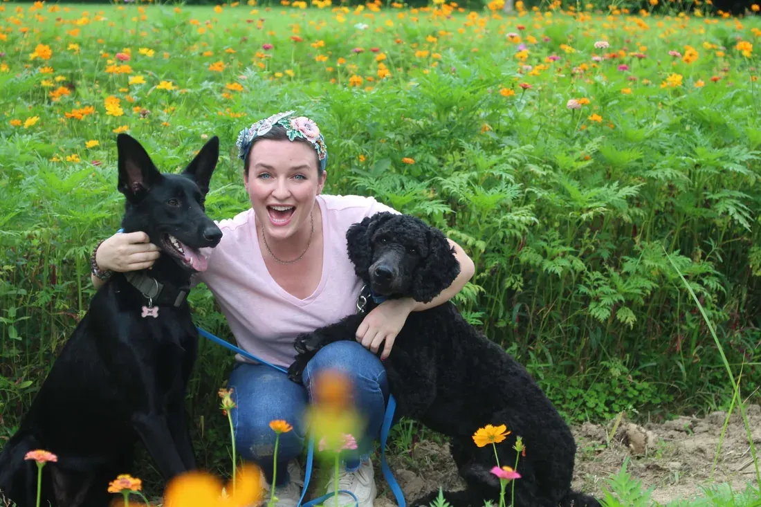 Claire Kane kneeling in a field of wildflowers with her arms around two of her dogs